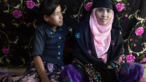 Tahera sitting with her daughter behind a bright backdrop, smiling at the camera